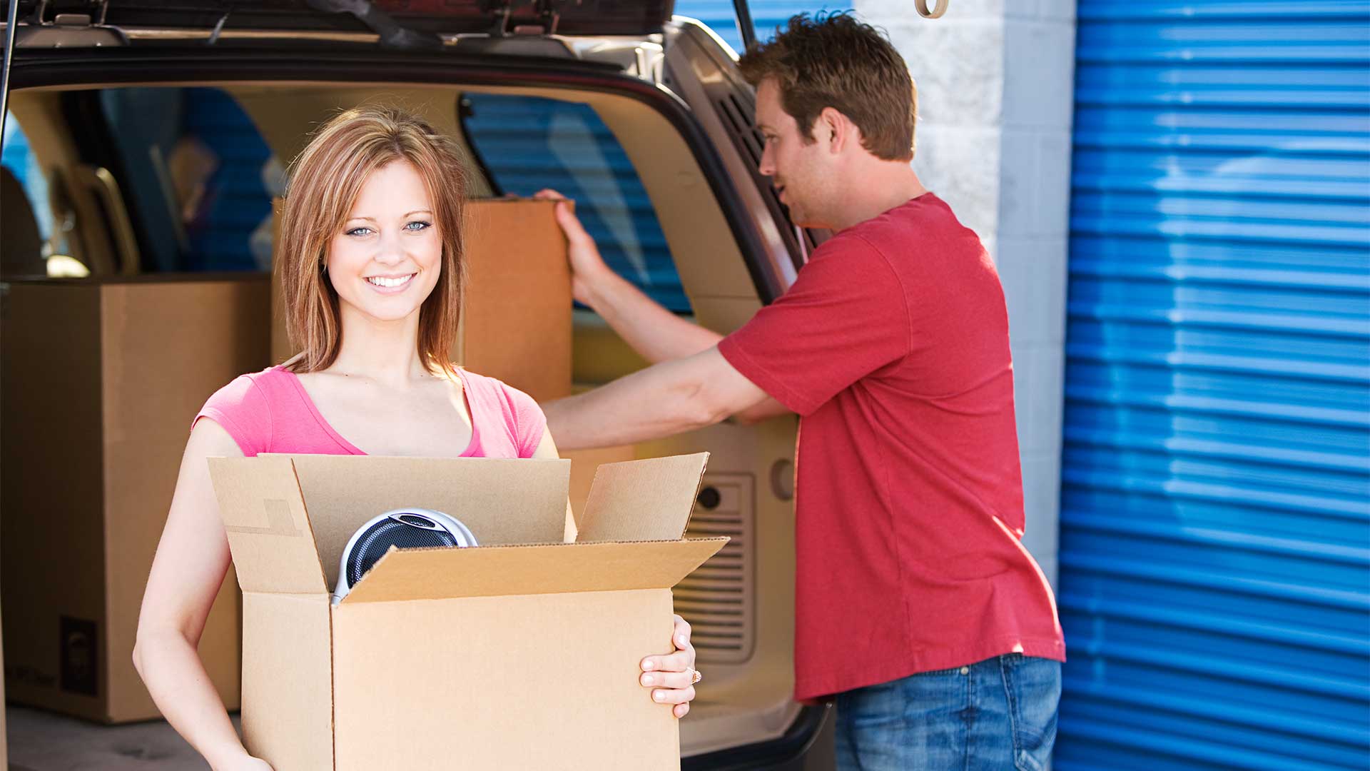 Woman and man unloading boxes from back of car for self storage